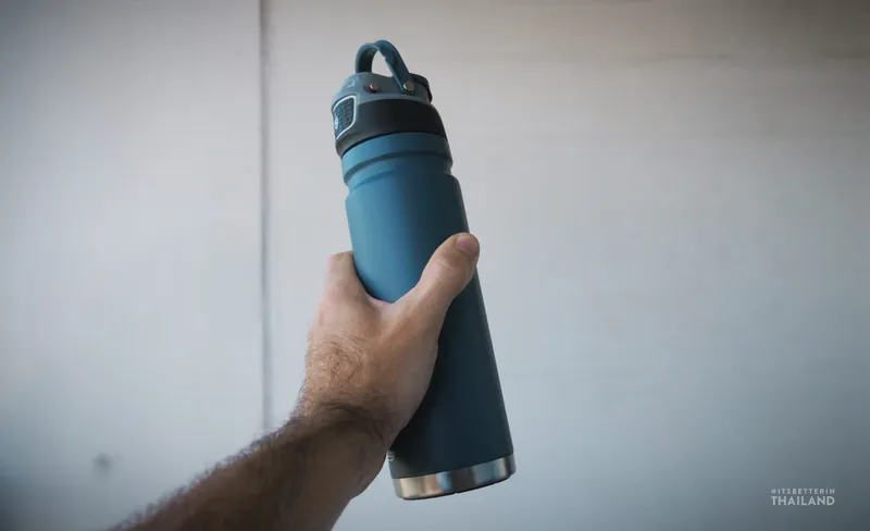 A reusable insulated water bottle held up against a white wall